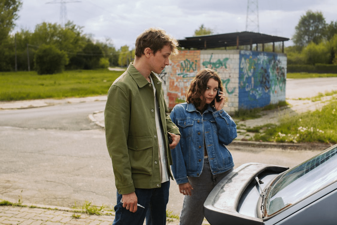 Two people stand beside a car that’s run out of fuel.
